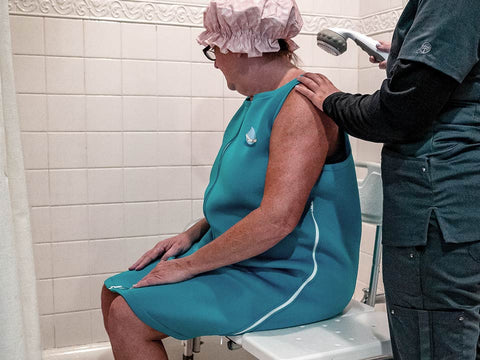 Une dame portant le vêtement de douche Blue hug qui se fait donner le bain assisté par une professionnelle de la santé